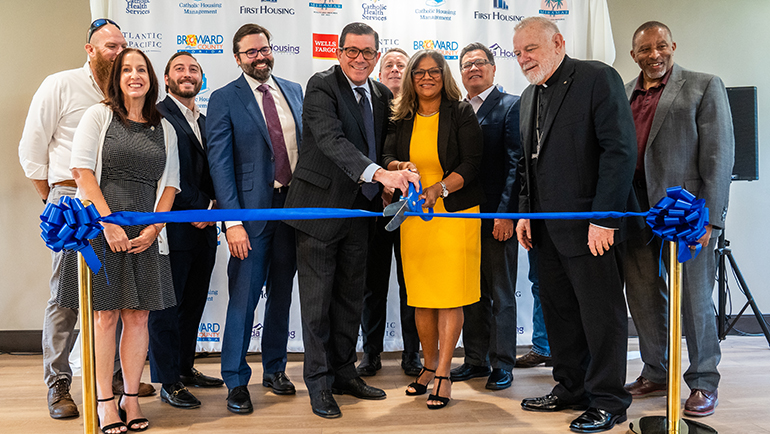 Ardy Pallin, presidente y director ejecutivo de Catholic Health Services, se prepara para cortar el listón con Juana D. Mejía, vicepresidenta de Desarrollo y Operaciones de Vivienda de Catholic Housing Management, en la dedicación de la Casa Sant'Angelo en Miramar, el 11 de agosto de 2023, ante la mirada del Arzobispo Thomas Wenski, invitados y funcionarios.