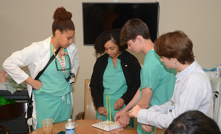 Drs. Anniki Witter and Ashli Alexander teach Cardinal Gibbons High School students Vincent Perez and Jack Perez how to perform surgical knot tying.