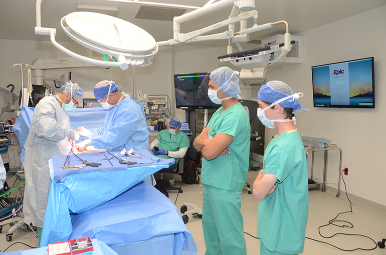Dr. Nathan Schoen, cofounder of the Summer Surgical Scholars program and chief resident, University of Miami at Holy Cross; Dr. Francisco Bermudez, attending general surgeon; and Cardinal Gibbons High School student Jack Perez observe a unique combined laparoscopic and open surgery.