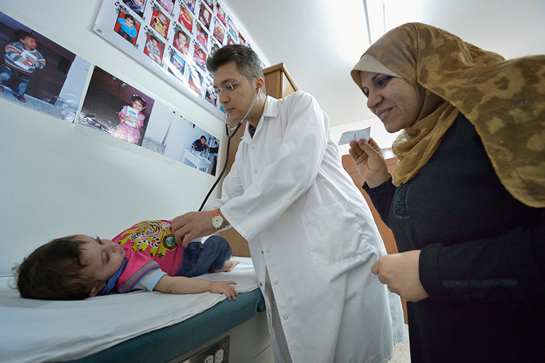 As the mother attempts distraction, Dr. Mohi El Sharqawi examines a child in the pediatric department at the CNEWA-supported al-Ahli Arab Hospital in Gaza City in 2015. Gaza Health Ministry said at least 500 people were killed Oct. 17, 2023, in the rocket on the hospital. (OSV News photo/Paul Jeffrey)