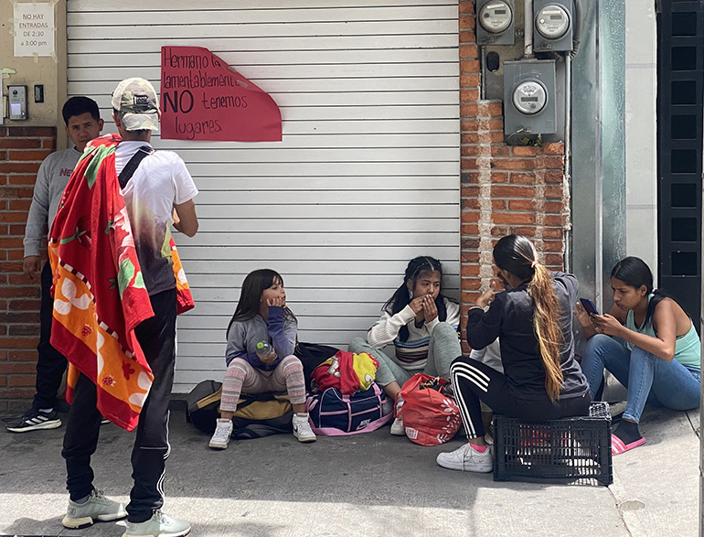 Migrants rest outside the CAFEMIN shelter in Mexico City Aug. 24, 2023, near a sign on the door that says there is no more room inside. With the growing number of migrants heading toward the U.S., shelters along the route from South America to the U.S. southern border are beyond capacity to help. (OSV News/photo/Rhina Guidos, Global Sisters Report)