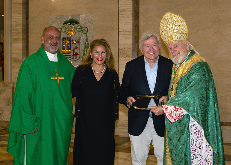 Archbishop Thomas Wenski gives the One in Charity Award to Diane and Jim Schurman, as their St. Ambrose pastor, Father Dariusz Zarebski, stands with them. They were one of three local Catholics honored at the annual ThanksforGiving Mass, which Archbishop Wenski celebrated Nov. 18, 2023.