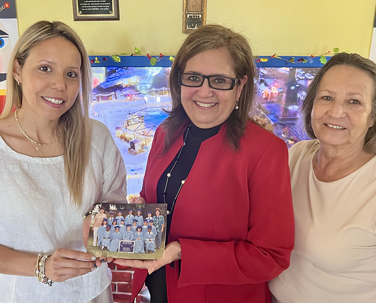Former student Alejandra Presiga, left, her mother Oliva Presiga, far right, and former pre-K teacher Otilia Penczak gathered at Good Shepherd Child Care Center in Cutler Bay on Dec. 7, 2023 to reminisce about their inspiring story. Alejandra and Penczak hold a photograph of Alejandra’s graduation from Good Shepherd in the early 1990s, in which Penczak is also pictured.