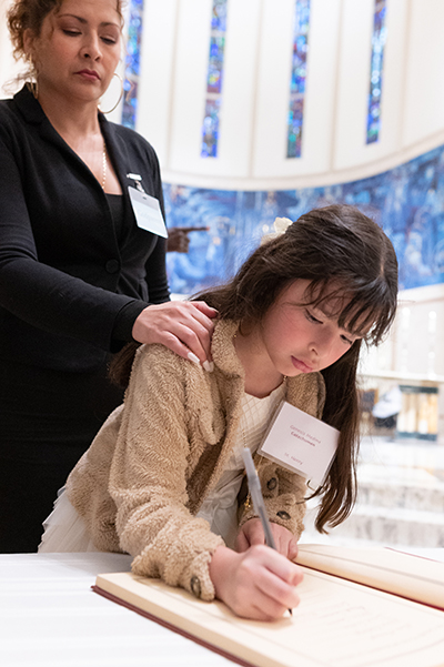 Godparent Olga Garcia of St. Henry Parish in Pompano Beach stands by as catechumen Genesis Medina signs the Book of the Elect containing the names of those who will soon join the Catholic Church, during the second of two Rite of Election ceremonies held at St. Mary Cathedral the Sunday after Ash Wednesday, Feb. 18, 2024.