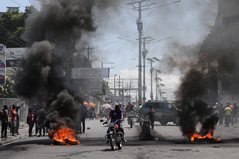 Motorists passed a burning barricade March 7, 2024, during a protest in Port-au-Prince, Haiti, as the government said it would extend a state of emergency for another month after an escalation in violence from gangs seeking to oust Prime Minister Ariel Henry. On March 11, Henry resigned after weeks of mounting chaos in the Caribbean nation.
