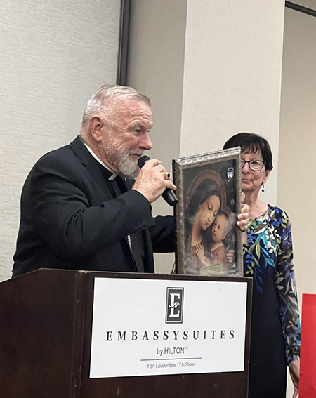 Archbishop Thomas Wenski shows an image of Our Lady of Good Counsel, the National Council of Catholic Women patroness, that he received from Mary Weber (right), chair of the MACCW Scholarship Committee. Archbishop Wenski was this year's honoree for his dedication to Catholic education in the Archdiocese of Miami on Feb. 24, 2024, in Fort Lauderdale.