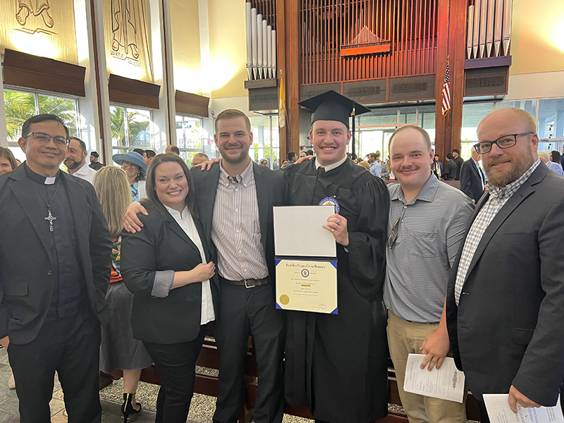 Seminarian Blake Schuman of the Diocese of Charleston holds his Bachelor of Arts in Philosophy diploma as he poses with his family and Father Raynier Q. Dabu, CRS (left) after Commencement Ceremony May 8, 2024, at St. John Vianney College Seminary. Twelve graduates received their diplomas at the Commencement Ceremony following the Baccalaureate Mass at St. Raphael Chapel. Supporting Schuman were his mother Jessica, brothers Zackary and Cole, and father Jesse.