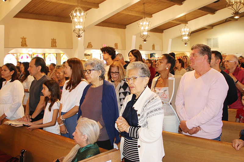 Parishioner Rita Frohlich, front right, joyfully worships at Mass on Dec. 8 at St. Matthew Church celebrated by Archbishop Wenski to bless the sanctuary, which received new marble flooring and altar furniture and restored amber wood.