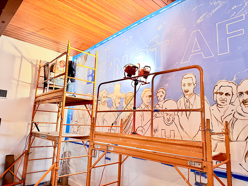 Behind the scenes photo of artist Jorge Rodriguez-Gerada working on scaffolding.