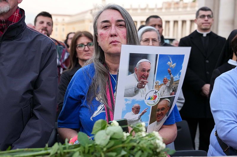 Una mujer sostiene un collage de imágenes del Papa Francisco y un ramo de flores mientras la gente se reúne en la Plaza de San Pedro para rezar por el Papa fallecido en el Vaticano, el 21 de abril de 2025. El Papa Francisco falleció esa misma mañana a las 7:35 hora local.