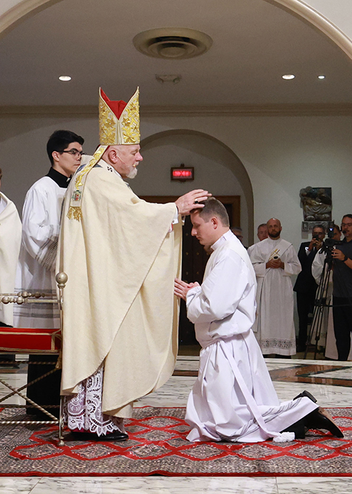Archbishop Thomas Wenski lays hands on Deacon Jakub Bereza, one of two men he ordained to the priesthood for the Archdiocese of Miami, May 10, 2025, at St. Mary Cathedral.
