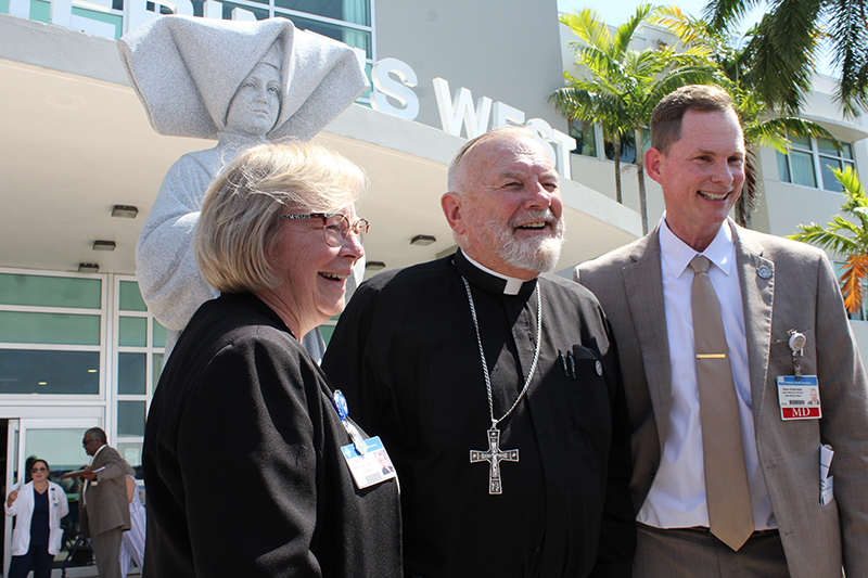 Archbishop Thomas Wenski posed with Mary Jo Frick, president and CEO of Catholic Health Services, and Dr. Brian Kiedrowski, chief medical officer of St. Catherine's West Rehabilitation Hospital in Hialeah Gardens, after the unveiling and blessing of the new St. Catherine Labouré statue seen behind them.