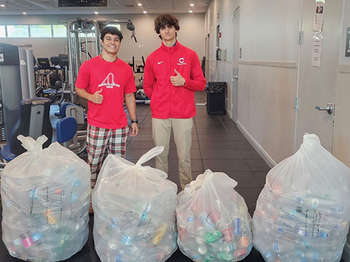 Christopher Columbus High School students Joshua Fernandez (left) and Julian Aviles pose Dec. 16, 2024, with trash bags filled with materials such as cans and bottles, which the high school students recycled as part of the Battle of the Bins competition against Our Lady of Lourdes Academy girls' school.