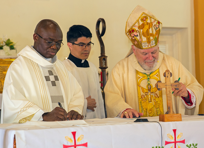 Archbishop Thomas Wenski and Spiritan Father Fidelis Nwankwo sign documents declaring Father Nwankwo the new pastor of St. Philip Neri Church in Miami Gardens, as Father Agustin Estrada, secretary of the archbishop, looks on June 22, 2025.