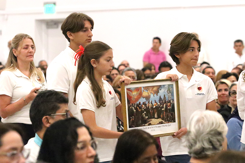 During the Mass celebrating the Great Vigil in Honor of the Two Hearts of Jesus and Mary on June 27, 2025 at Our Lady of Guadalupe Parish in Doral, young supporters of the Servants of the Pierced Hearts of Jesus and Mary take up an image symbolizing the new pastoral year for the Servants: 'Like the early Church, let us live in the power of the Holy Spirit."