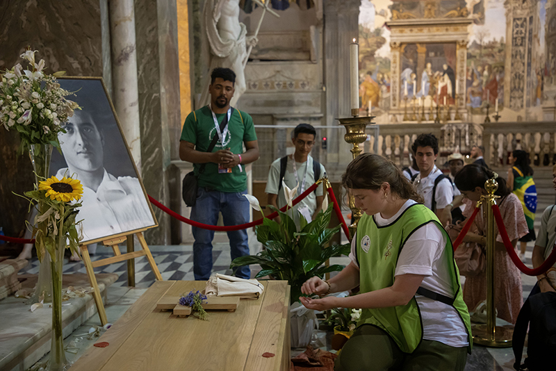 A volunteer places devotional items from pilgrims on the casket of Blessed Pier Giorgio Frassati at the Basilica of Santa Maria sopra Minerva in Rome July 31, 2025. The items, including rosaries and prayer cards, are temporarily laid on the casket to become third-class relics before being returned to their owners.