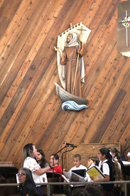 El coro del colegio de St. Brendan, Miami, cantan durante la Misa el 3 de sept., 2025, celebrando 70 años desde la fundación del colegio. Arriba del coro, se ve una imagen de Santo Brendan en un barco. El santo irlandés se reconocía por su trabajo misionero, y a veces lo llamaban 'Brendan el Navegador.'