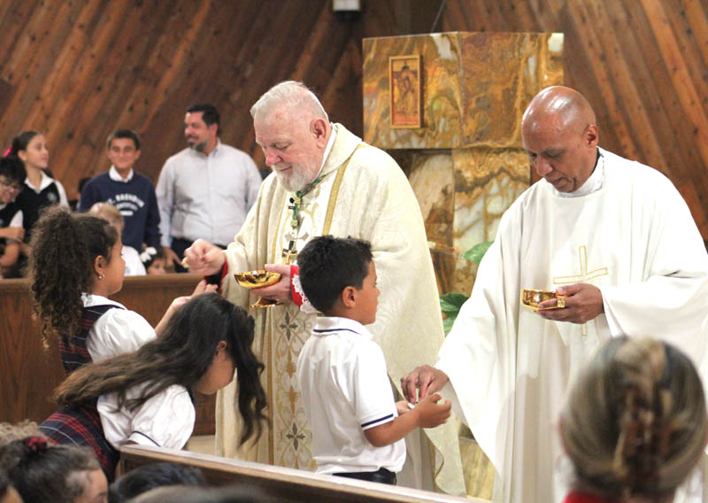 Arzobispo Thomas Wenski y el Padre Miguel Sepúlveda, párroco de la parroquia de St. Brendan, Miami, distribuyen la Comunión a los estudiantes durante una Misa el 3 de sept., 2025, celebrando el 70 aniversario del colegio de St. Brendan.