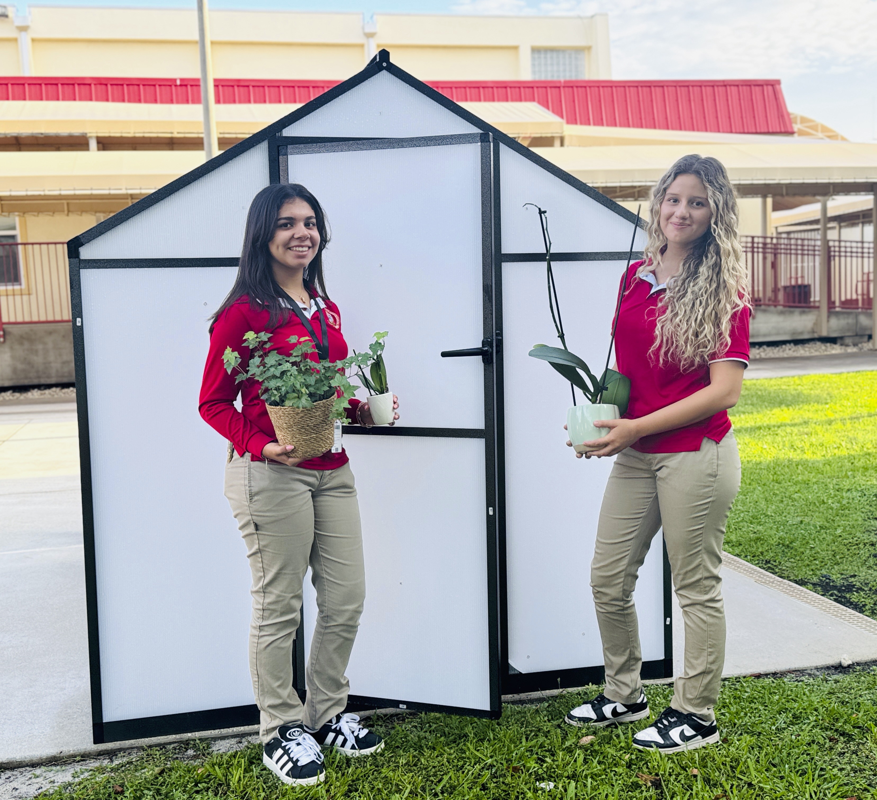Emilie Alvarez (left) and Angelina Vargas, co-founders of Monsignor Edward Pace High School’s Evergreen Club, smile for the camera outside the newly constructed greenhouse during the fall 2025 semester.