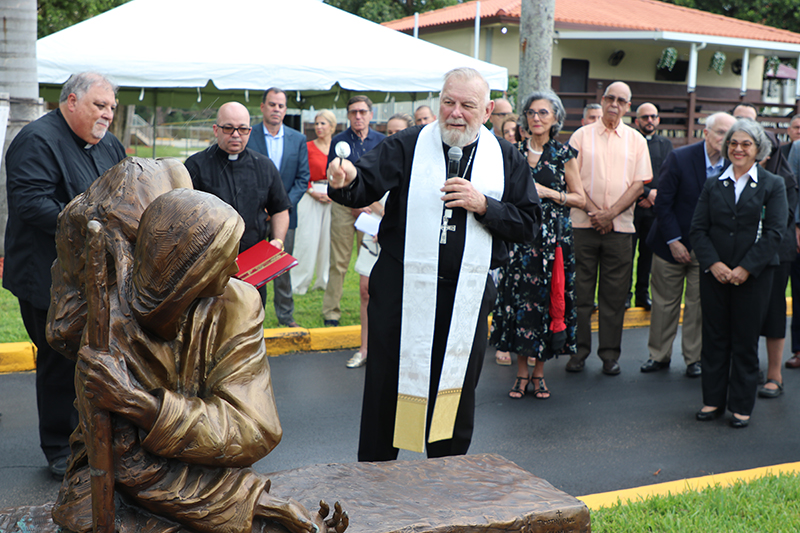 El Arzobispo Thomas Wenski bendice la escultura Be Welcoming, el 22 de agosto en La Ermita de la Caridad. Be Welcoming es una de dos esculturas creadas por Timothy Schmalz en honor a los inmigrantes y refugiados que fueron donadas a la arquidiócesis por Mike Fernández.