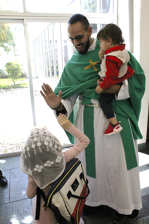 After a Mass celebrated at St. Rafael Chapel at St. John Vianney College Seminary in Miami for participants of the Bridging the Gap Conference on Sept. 26, 2025, Piarist Father Ricardo Rivera, principal of St. John the Apostle School in Hialeah, high-fives Galyana Cruz while carrying her brother, Giore'.