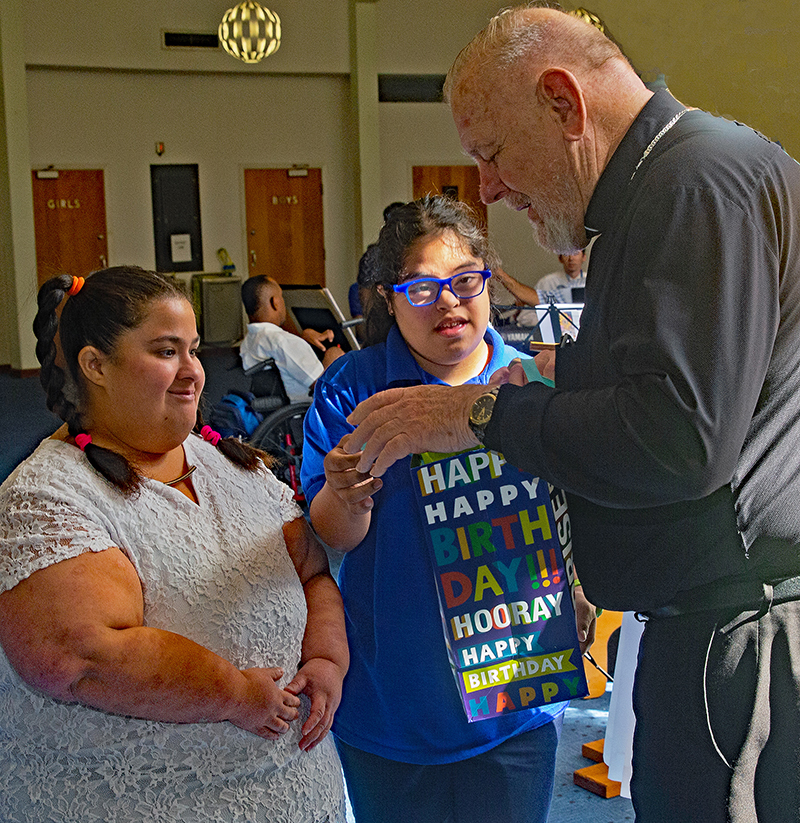 From left, Ruth Paz, part of the adult program at the Marian Center, and student Alyssa Rodriguez give Archbishop Thomas Wenski, whose birthday was Oct. 18, a pair of socks commemorating Down Syndrome Awareness Month Oct. 21, 2025.