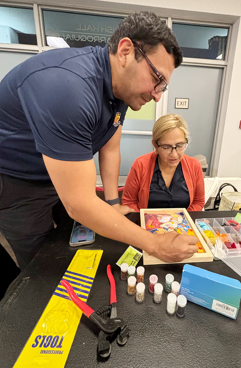 El P.  Alexander Narváez, quien imparte el taller de Arte Sacro en la parroquia Our Lady of Guadalupe, le da indicaciones en la técnica de mosaico a Carolina Angola, una participante del taller, en una clase en octubre de 2025.
