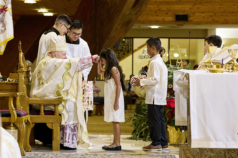 Archbishop Thomas Wenski blesses a little girl who presented him a gift  Dec. 23, 2025. She was one of several children who bore gifts during the Simbang Gabi Mass at St. David Church in Davie.