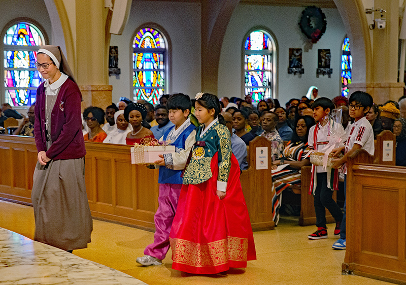 Sister Mary Martha Cuenca of the Servants of the Pierced Hearts of Jesus and Mary, leads children carrying gifts to Archbishop Thomas Wenski during the offertory of the annual Migration Mass celebrated Jan. 11, 2026, feast of the Baptism of the Lord, at St. Mary Cathedral.