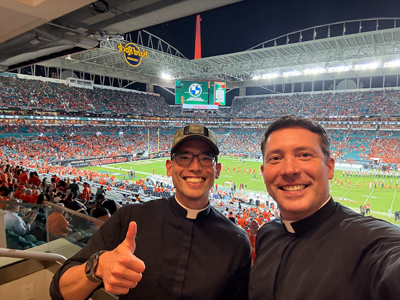 Father Richard Vigoa, right, pastor of St. Augustine Church in Coral Gables, poses for a selfie with Father Adam Tokashiki, chaplain of the University of Miami Catholic Student Center, at a University of Miami Hurricanes football game at Hard Rock Stadium in Miami Gardens were the national championship game between the University of Miami Hurricanes and the Indiana Hoosiers will take place Jan. 19, 2026.