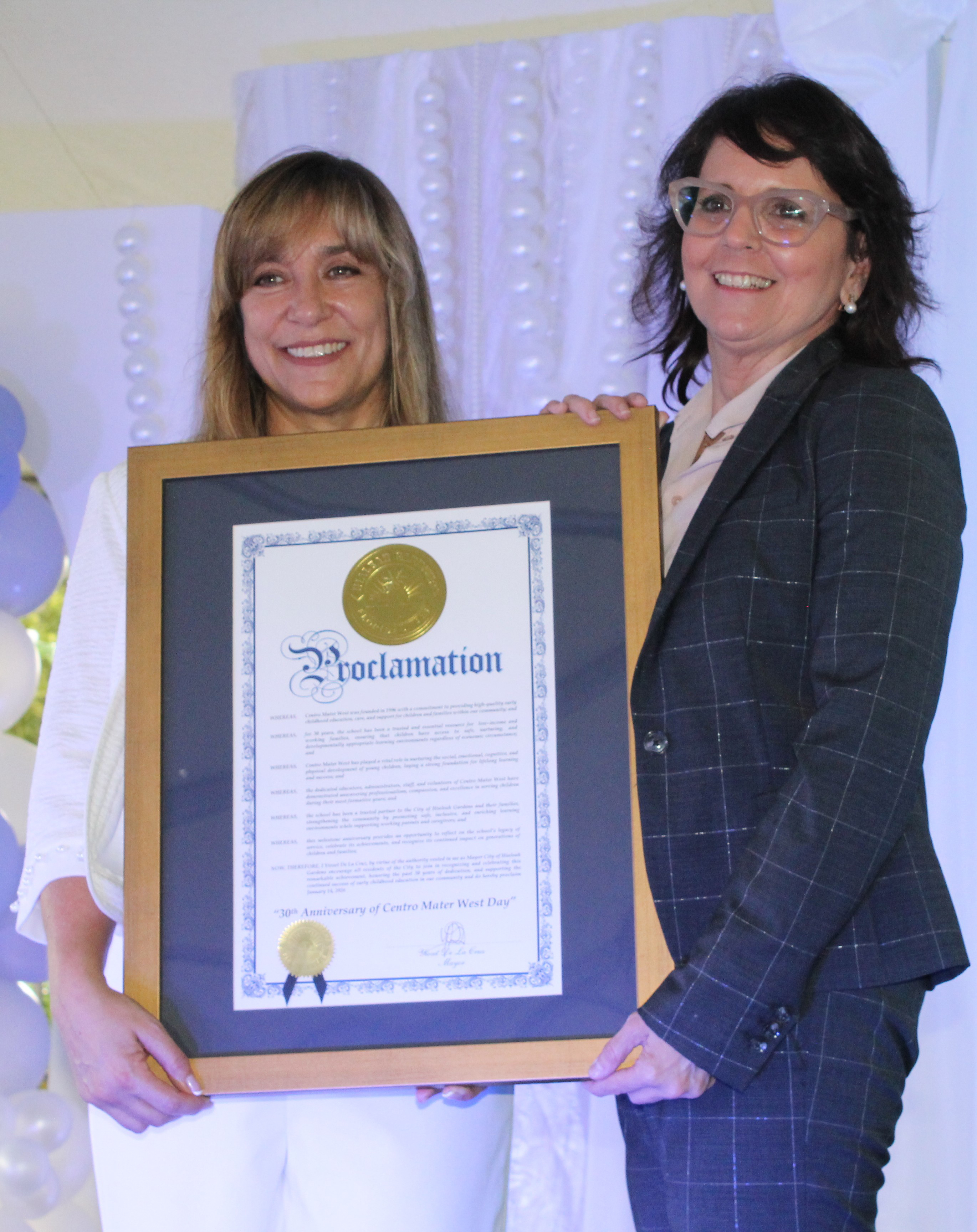 Julietta Riveron (left), Centro Mater West Program Administrator, and Madelyn Llanes, Centro Mater Exectuive Director, hold up a proclamation given to Centro Mater West on behalf of the City of Hialeah Gardens and Mayor Yioset de la Cruz during the Centro Mater West Child Care center's 30th anniversary celebration on January 14, 2026.