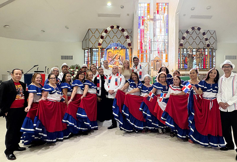 El P. Wilfredo Contreras (centro izquierda), párroco de la iglesia San Isidro, posa para la foto con un grupo de damas y caballeros dominicanos vistiendo sus trajes típicos dominicanos, después de la celebración de la Virgen de La Altagracia, en la parroquia de en Pompano Beach, el 17 de enero de 2026.