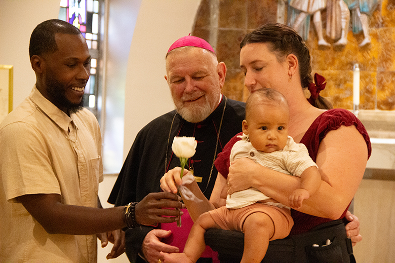 Zachary (left) and Nicole Burgh and their baby, Ezra, get ready to take a photo with Archbishop Thomas Wenski at the Archdiocese of Miami Wedding Anniversary Mass at the Cathedral of St. Mary Feb. 21, 2026. Zachary and Nicole are celebrating their first anniversary.