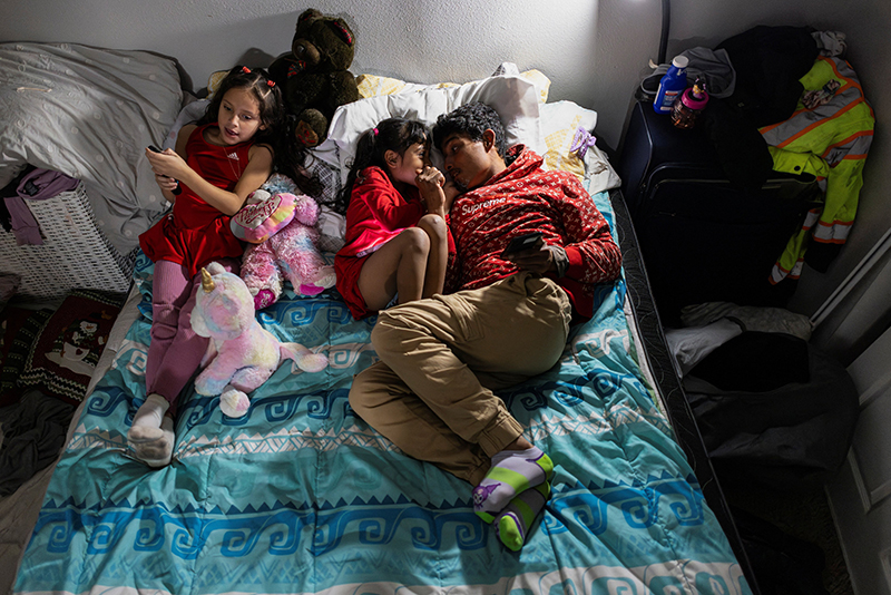 A Venezuelan migrant man lies in bed with his daughters in Aurora, Colo., Jan. 30, 2025. Despite having legal documentation to reside in the U.S., the family feared reports that U.S. Immigration and Customs Enforcement agents may come to detain immigrants even with documents for deportation. (OSV News photo/Kevin Mohatt, Reuters)