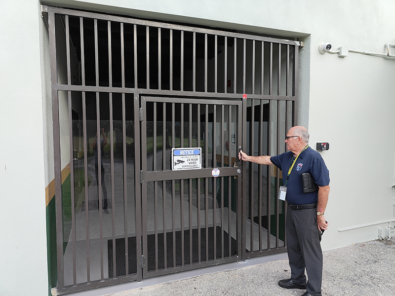 A locked security gate provides controlled access between the athletic fields and the main campus at St. David Catholic School. The area is monitored by surveillance cameras as part of the school's layered approach to campus safety.