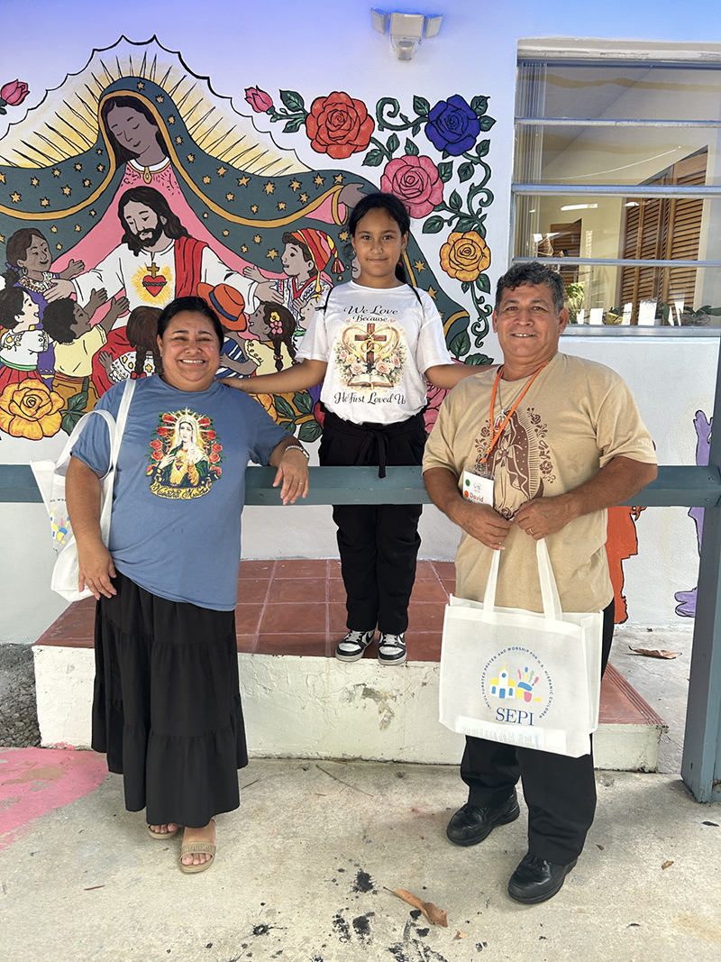 Desde la izquierda, Juanita Valdivia; su hija, Estefany Murillo y su esposo David Murillo, feligreses de la parroquia St. Michael the Archangel en Miami, posan delante del mural “Dejen que los ni&ntilde;os vengan a m&iacute;”, en el Instituto Pastoral del Sureste para el Ministerio Hispano, SEPI, el 26 de julio. La familia particip&oacute; en la primera conferencia de la Pastoral Infantil realizada en el SEPI del 24 al 26 de julio de 2026.