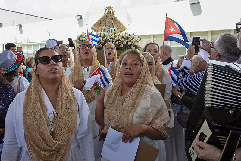 (Center/back) Carla Salazar, head of "Las Cantoras Nazarenas,” sings to welcome the pilgrim image of Our Lady of Charity at St. Louis Parish in Pinecrest Aug. 22, 2026, during a 35-mile motorcade procession through Miami-Dade County. Parishioners gathered with Cuban flags, prayers and cellphones as the image – a symbol of the Virgin Mary’s presence in South Florida – arrived at the third of nine parish stops.