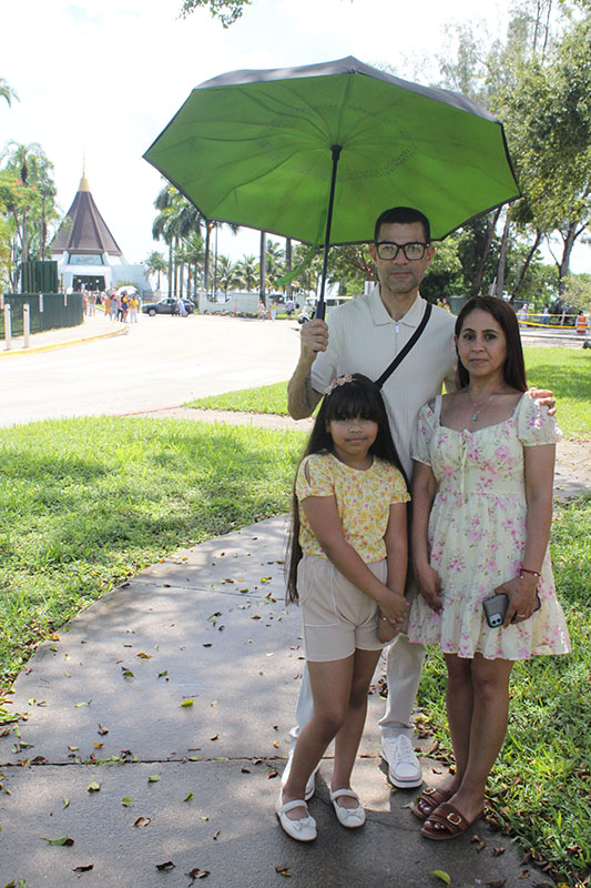 Iraida Lopez and Raynier Martinez stand with their daughter Natalia after visiting the National Shrine of Our Lady of Charity in Miami (seen left in the background) on Sept. 7, 2026. Our Lady of Charity is known as the patroness of Cuba, and many Cubans living in Miami maintain a devotion, with thousands visiting the shrine year-round, especially during the days leading to her annual feast day, Sept. 8.