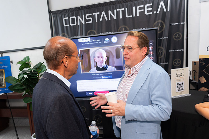 Scott Coloney, right, president and founder of ConstantLife – an artificial intelligence company based in Fort Lauderdale – demonstrates an AI-generated avatar of the late Father John O’Looney, who was first appointed pastor of St. Anthony Parish in 1929. The AI avatar was created for the centennial festivities at St. Anthony Catholic School in Fort Lauderdale Sept. 13, 2026.