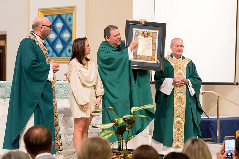 Father Rolando Cabrera, pastor of St. Anthony Parish, holds up a papal blessing document from Pope Leo XIV at St. Anthony School’s Centennial Mass at the parish in Fort Lauderdale Sept. 13, 2026. From left, standing with him are Father Carmelo Romanello, parochial vicar, Jenna McIntosh, principal of St. Anthony School, and Father Michael Grady, pastor emeritus.
