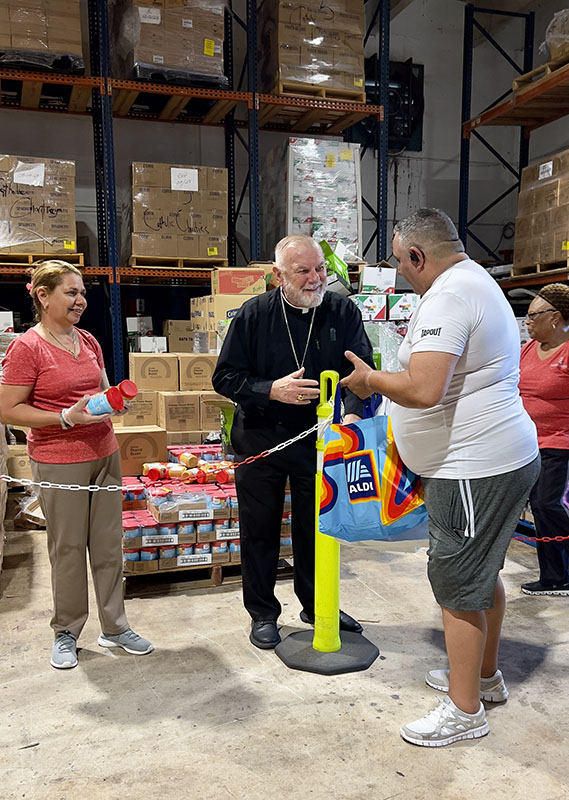 Archbishop Thomas Wenski smiles after he distributes goods to an individual who benefits from Matthew 25 Food Pantry in Miami, operated by Catholic Charities of the Archdiocese of Miami, Inc. Archbishop Wenski joined volunteers on a distribution Saturday, Aug. 15, 2026, where filming also took place for the 2027 Archbishop's Charities and Development Drive (ABCD) video.