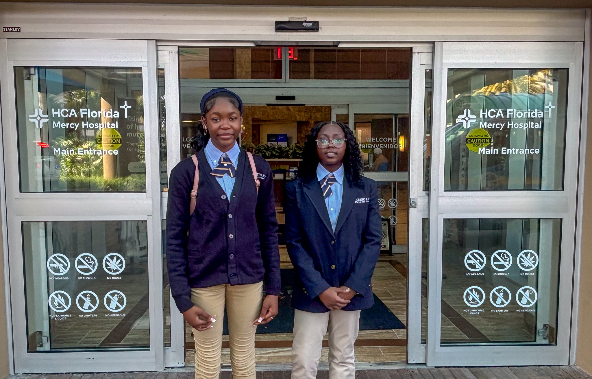Cristo Rey Miami High School ninth-graders Nailah Civil, left, and Marcelinesarah Senecharles take a snapshot outside HCA Florida Mercy Hospital in Miami, their new workplace, on Aug. 14, 2026. (COURTESY)