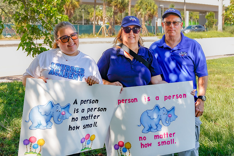 Margarita Cooper, a board member of the ARCH Angels of South Florida Catholic homeschool community, poses with her husband and daughter holding pro-life signs during the annual Miami Life Chain display across US 1 on Respect Life Sunday, Oct. 4, 2026.