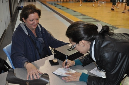 Gianna Lopez, whose daughter plays on the JV basketball team at Archbishop Carroll High School, signs a check as Teresa Pulido, Briana’s mom, collects the donations at the entrance to the gym.