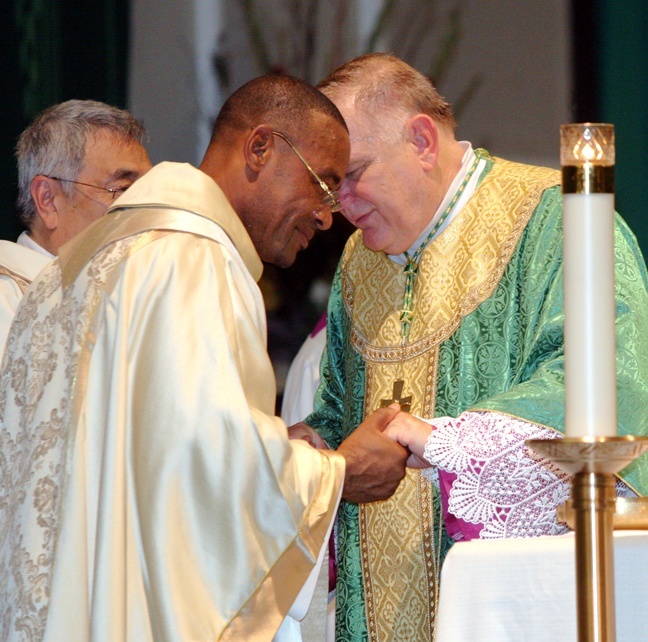 rchbishop Wenski exchanges the sign of peace with Father Robés Charles, pastor of St. Clement Church.