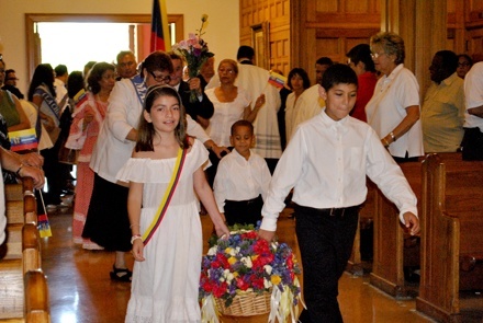 Children, dressed in traditional Colombian clothing, bring flowers up to the image at the start of Mass.