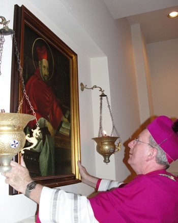 Auxiliary Bishop John Noonan hangs a painting of St. Robert Bellarmine on one of the walls of the church.