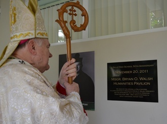 Archbishop Thomas Wenski pauses in front of the plaque that memorializes Msgr. Bryan O. Walsh on the original building of La Salle High School.