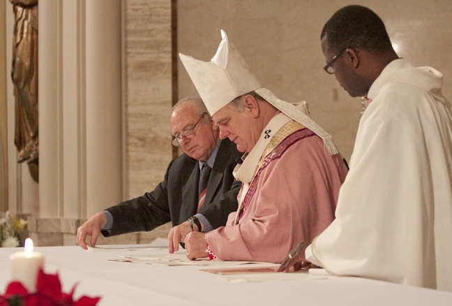 Archbishop Thomas Wenski signs the papers erecting Redemptoris Mater seminary. At left is Adelchi Chinaglia, canonist for the Neocatechumenal Way, and at right is Father Chanel Jeanty, archdiocesan chancellor for canonical affairs.