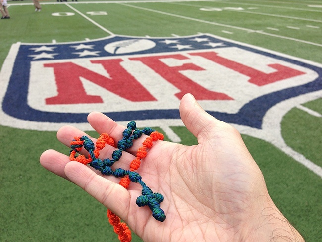 Father Manny Alvarez holds an aqua and orange rosary made by a St. Gregory parishioner, a rosary he prays while standing on the sidelines at Dolphins games.